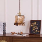 Clérachic pendant with a squared amber glass shade, unlit, hanging above a console with a gold-on-black framed print and books.