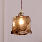 Clérachic pendant with a squared amber glass shade, lit, with a bright bulb visible through the swirled brown glass.