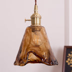 Close view of the flared amber glass shade and the brass switch holder on this Clérachic pendant, with a gold print blurred behind.