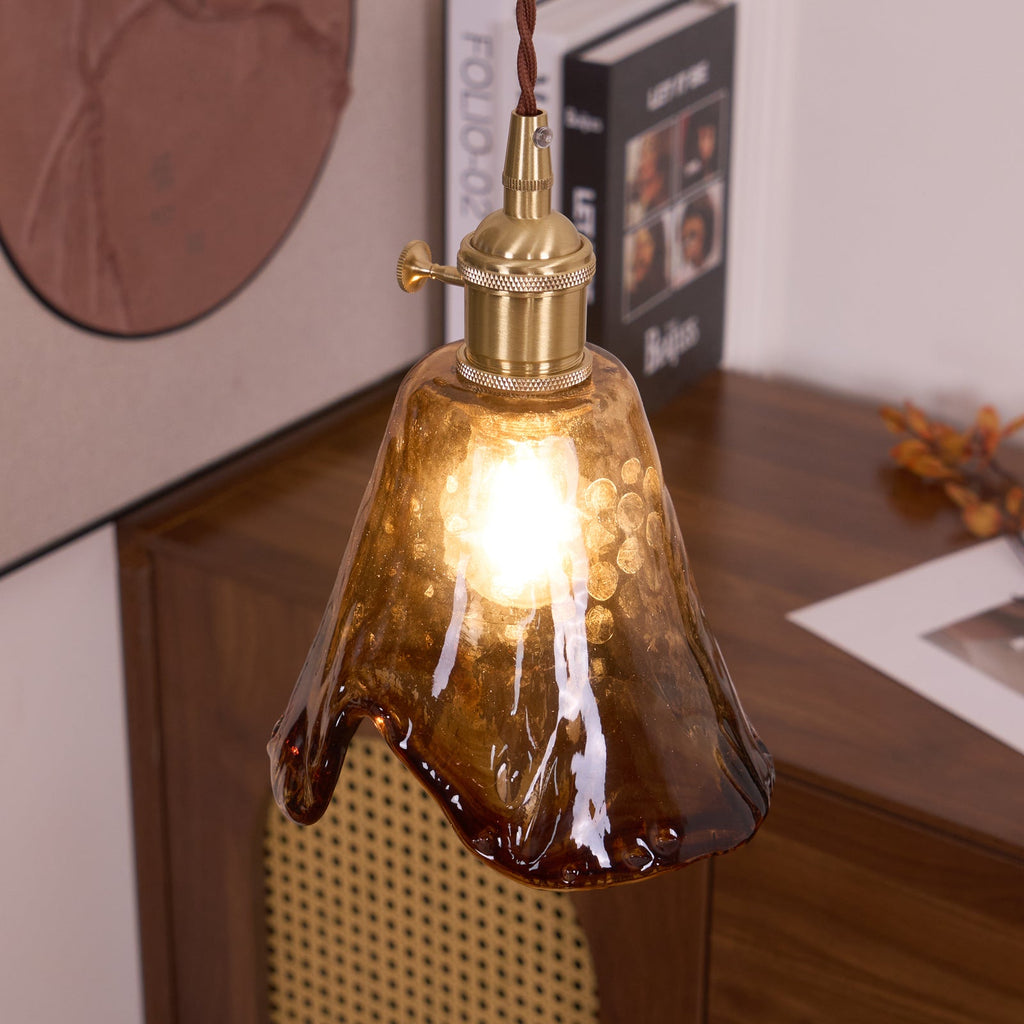 Clérachic pendant with a flared amber glass shade, lit, hanging in front of a round print and a cane-front cabinet.