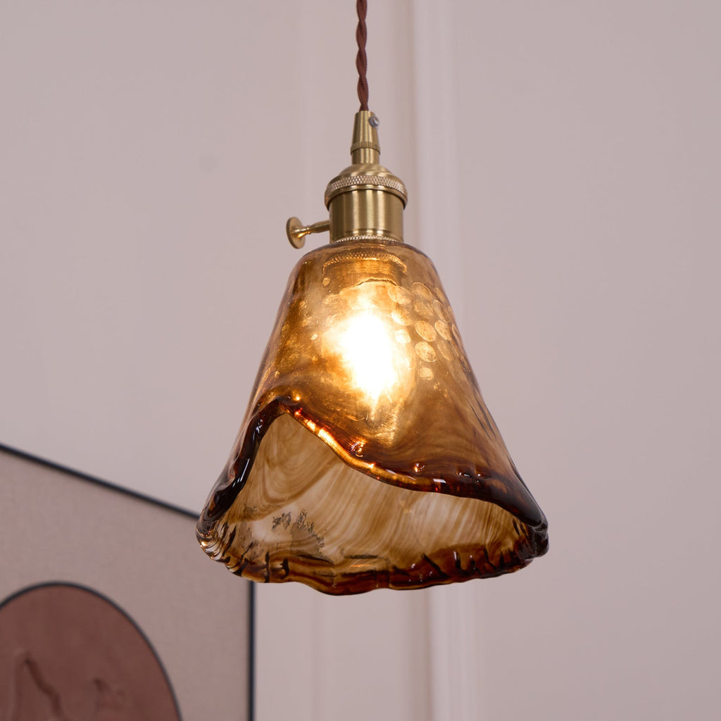 Lit Clérachic pendant with a flared amber glass shade, seen from slightly below, with its wavy rim and brass switch holder.