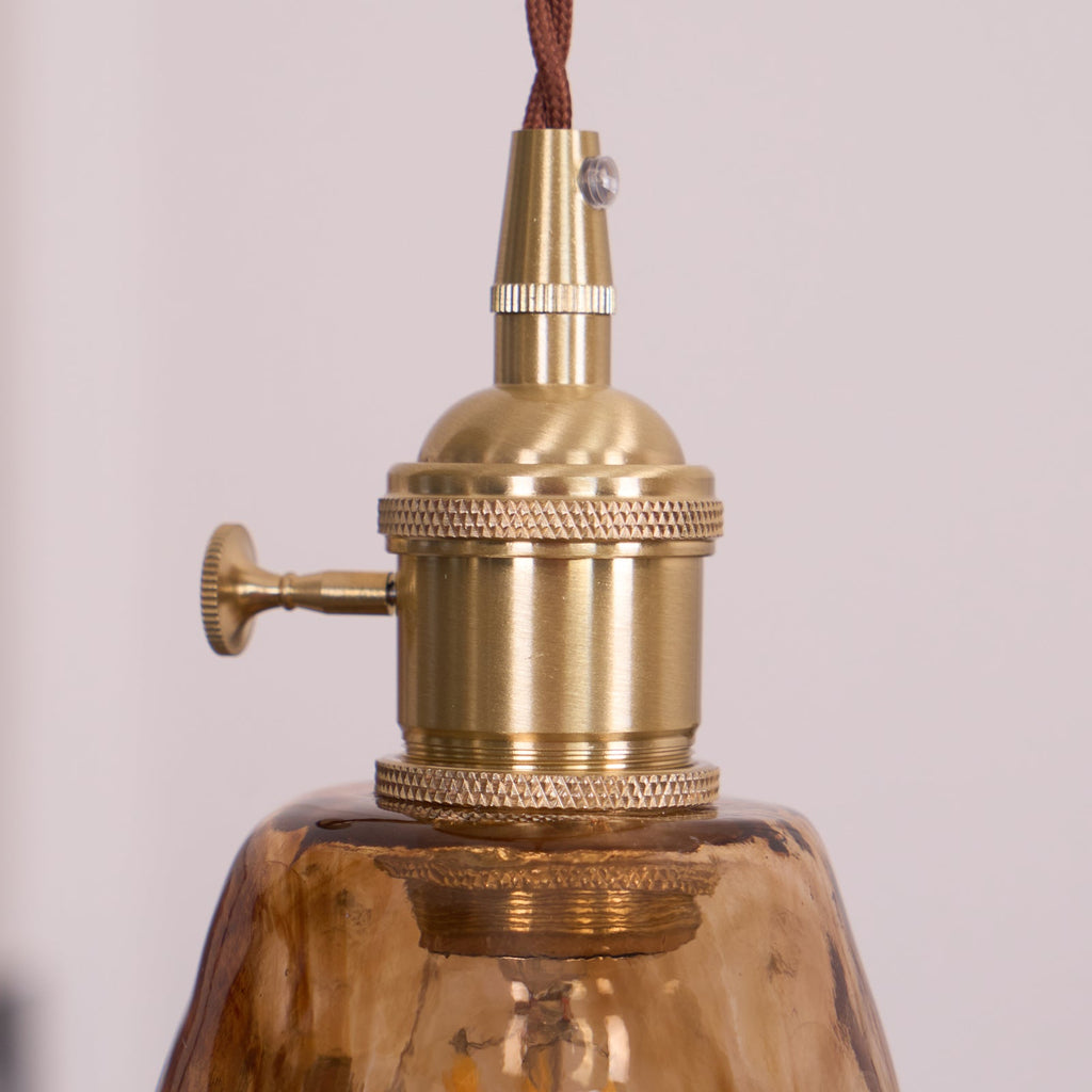 Close view of the knurled brass switch holder on this Clérachic pendant, with its small thumb switch and the amber shade below.
