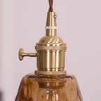 Close view of the knurled brass switch holder on this Clérachic pendant, with its small thumb switch and the amber shade below.