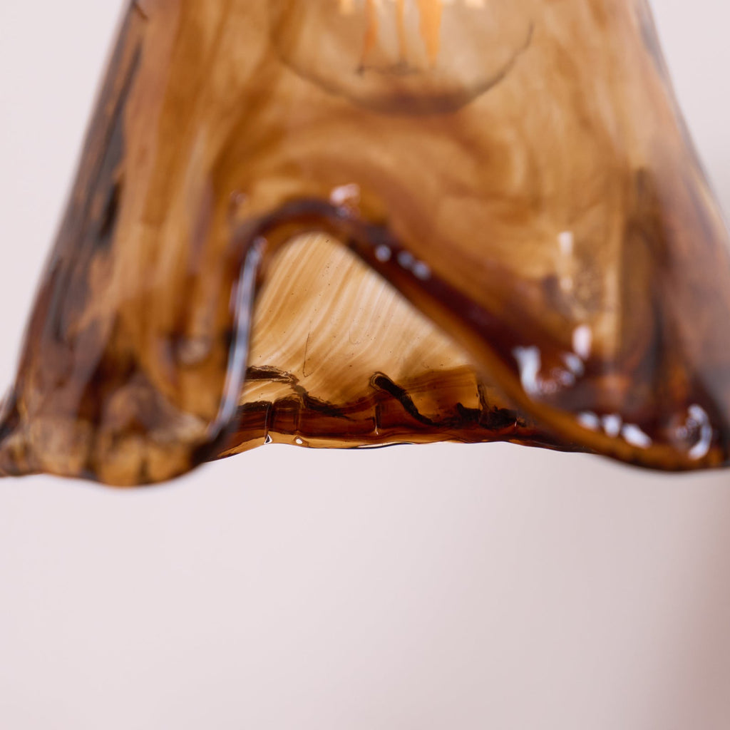 Close view of the swirled amber and dark brown glass at the hem of this Clérachic pendant's shade, lit from inside.