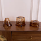 Three loose Clérachic amber glass shades on a walnut cabinet, with a flared, a squared and a round shape side by side.