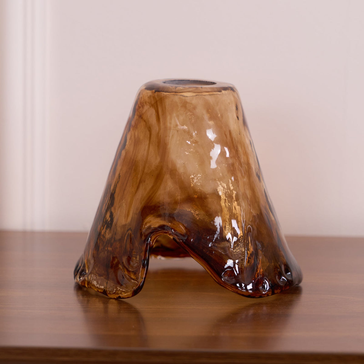 A loose flared Clérachic amber glass shade standing on a wooden surface, with its three-point hem and swirled brown glass.