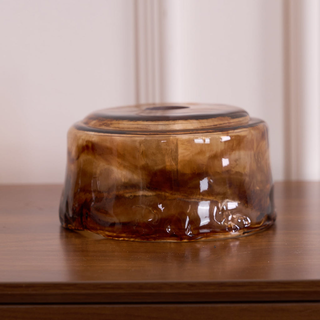 A loose low, round Clérachic amber glass shade on a wooden surface, with a swirled amber and brown pattern and a thick rim.