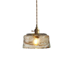 Clérachic pendant with a low, round amber glass shade, on a white backdrop, with a lit bulb and a brass switch holder.