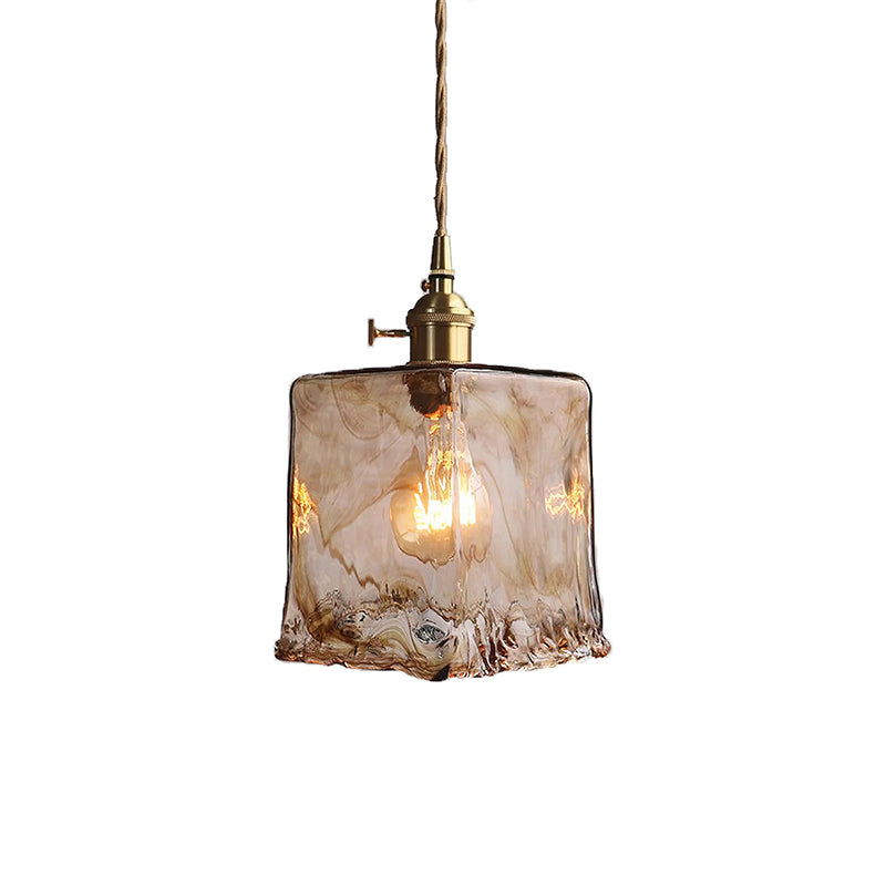Clérachic pendant with a squared amber glass shade, lit, on a white backdrop, with a twisted cord and a brass switch holder.