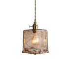 Clérachic pendant with a squared amber glass shade, lit, on a white backdrop, with a twisted cord and a brass switch holder.