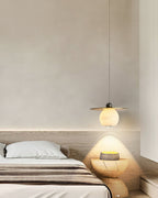 Clérachic Brass and Alabaster Globe Cord Pendant Light lighting a carved wood stool beside a low oak platform bed.