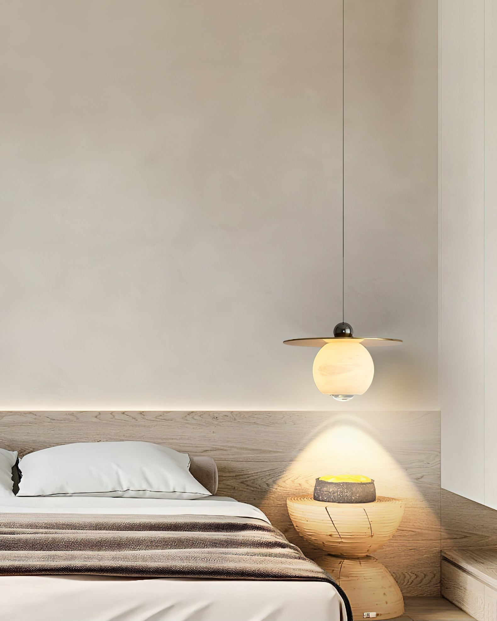 Clérachic Brass and Alabaster Globe Cord Pendant Light lighting a carved wood stool beside a low oak platform bed.