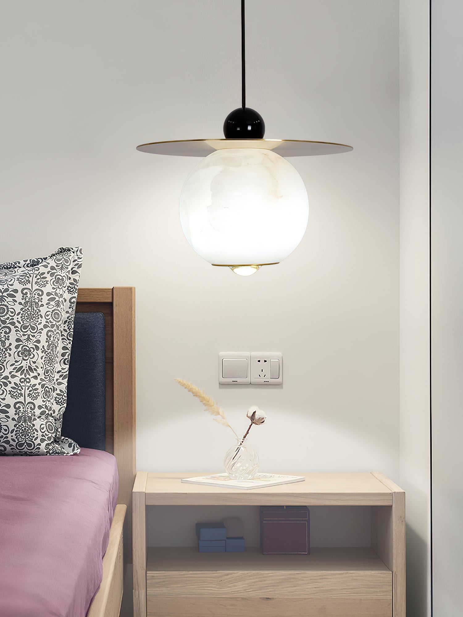 Clérachic Brass and Alabaster Globe Cord Pendant Light glowing above an oak nightstand and a dried cotton stem in glass.