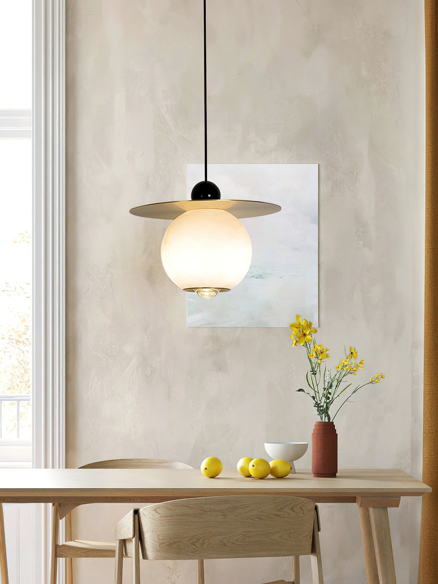 Clérachic Brass and Alabaster Globe Cord Pendant Light above a pale dining table set with lemons and yellow blooms.