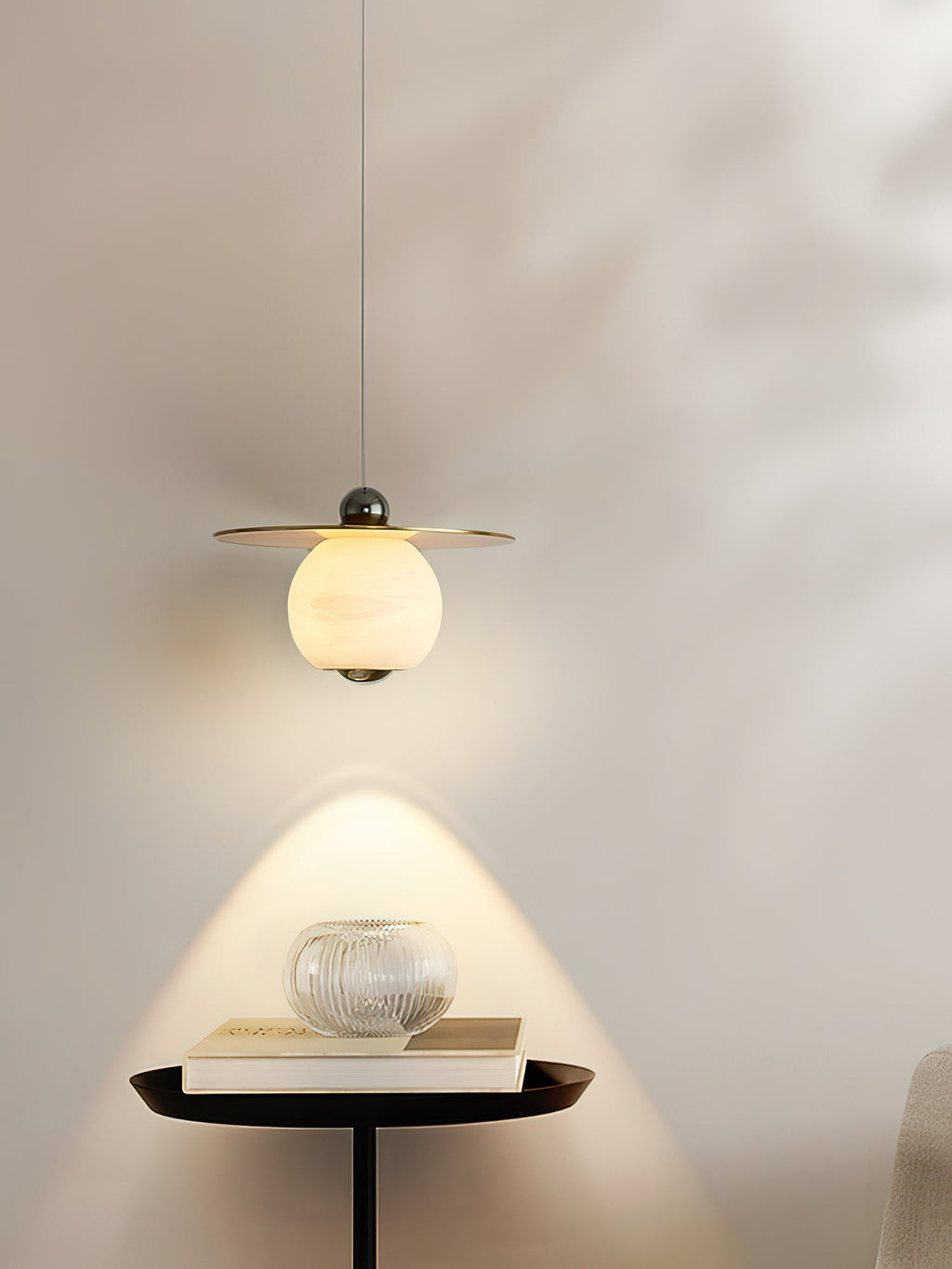Clérachic Brass and Alabaster Globe Cord Pendant Light lighting a black pedestal table with a book and ribbed glass bowl.