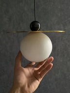 A hand cupped under the Clérachic Brass and Alabaster Globe Cord Pendant Light shows the globe is about palm-sized.