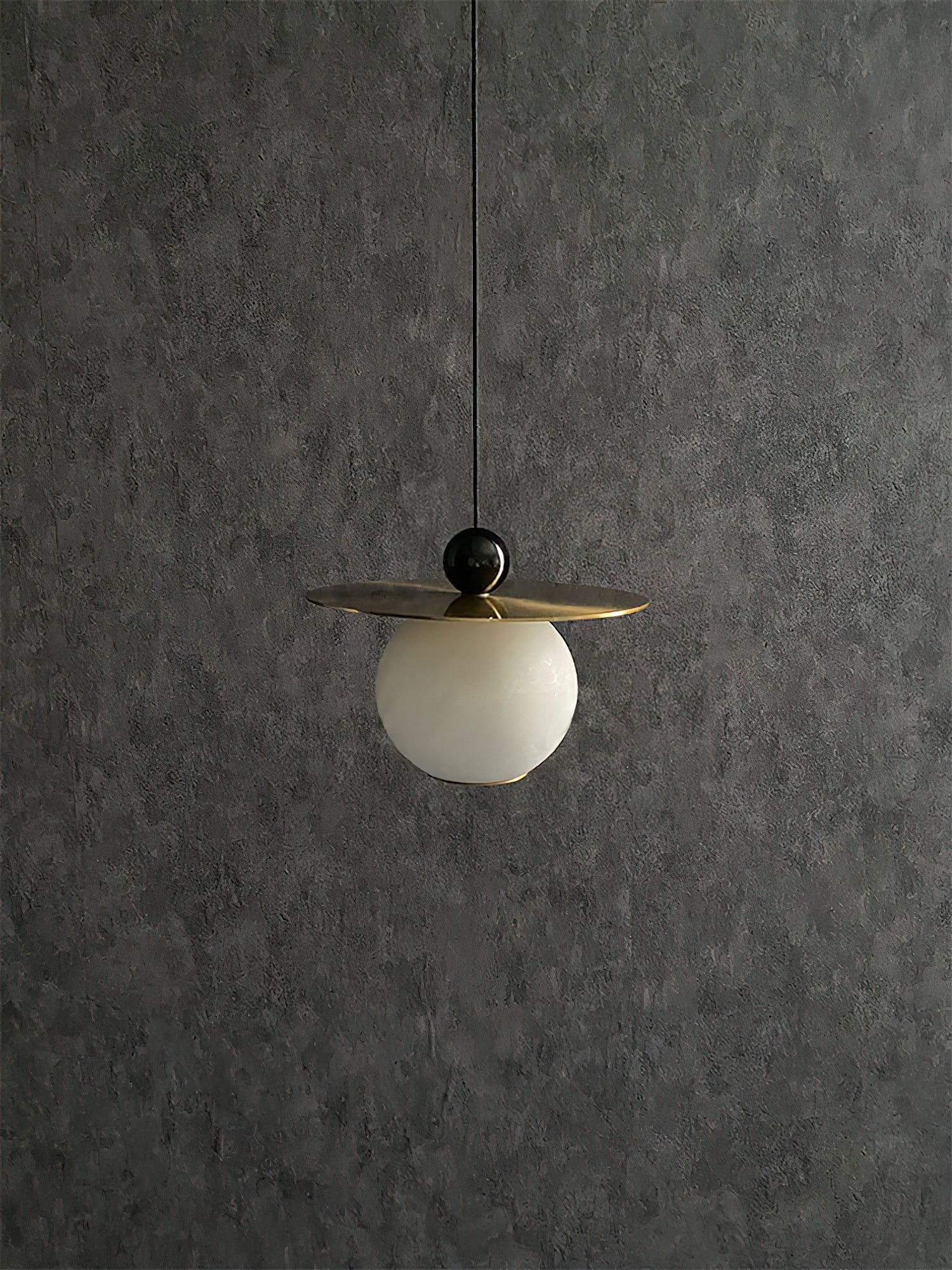 Clérachic Brass and Alabaster Globe Cord Pendant Light hanging switched off against a dark textured plaster wall.