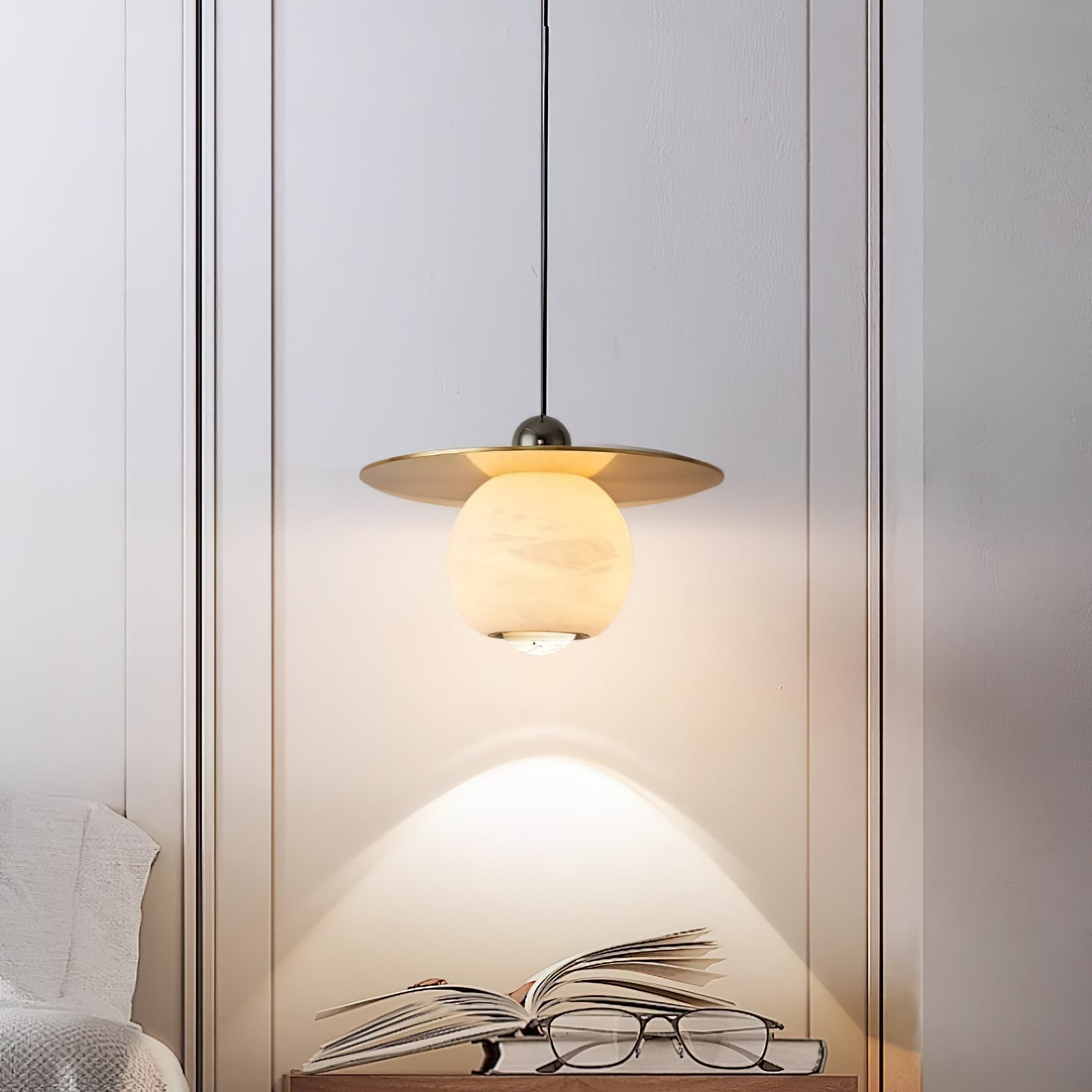 Clérachic Brass and Alabaster Globe Cord Pendant Light lighting an open book and reading glasses on a bedside table.