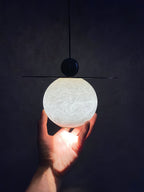 The lit Clérachic Brass and Alabaster Globe Cord Pendant Light held in one hand, veining glowing through the stone.