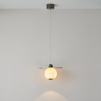 Clérachic Brass and Alabaster Globe Cord Pendant Light lit on its full cord drop, pooling warm light on the wall below.