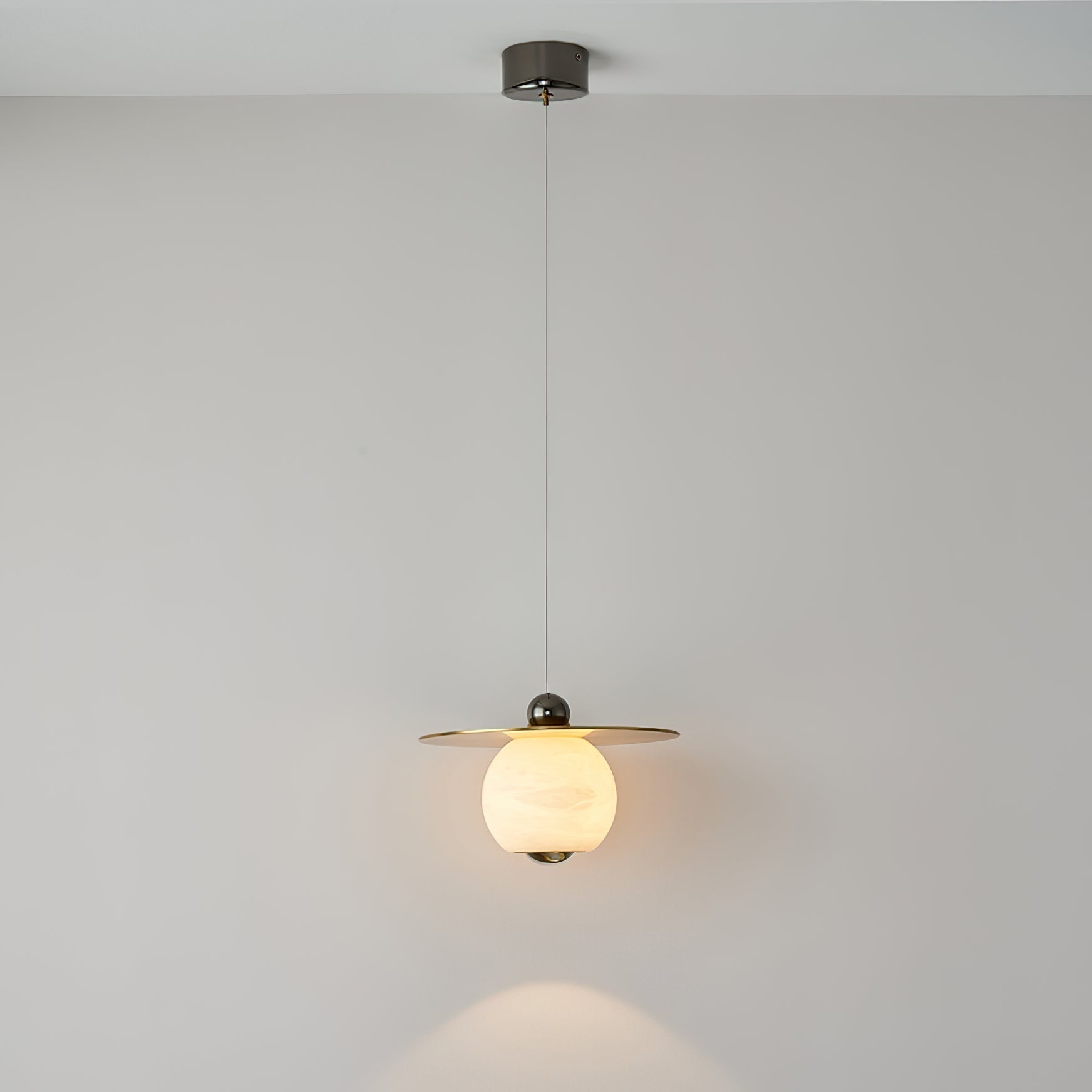 Clérachic Brass and Alabaster Globe Cord Pendant Light lit on its full cord drop, pooling warm light on the wall below.