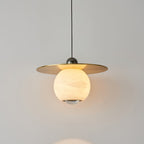 Clérachic Brass and Alabaster Globe Cord Pendant Light lit, warm light bouncing off the underside of the brass disc.
