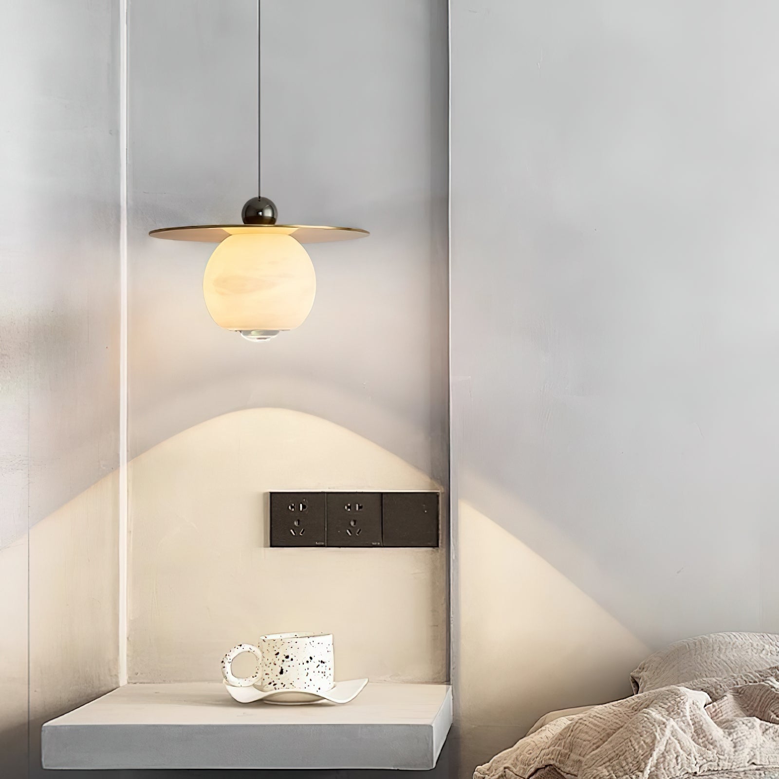 Clérachic Brass and Alabaster Globe Cord Pendant Light lighting a plaster alcove ledge with a speckled ceramic cup.
