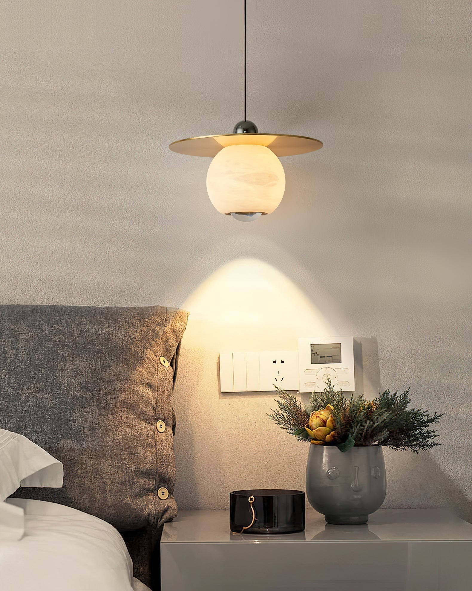 Clérachic Brass and Alabaster Globe Cord Pendant Light lighting a bedside top with a face-motif planter and glass jar.