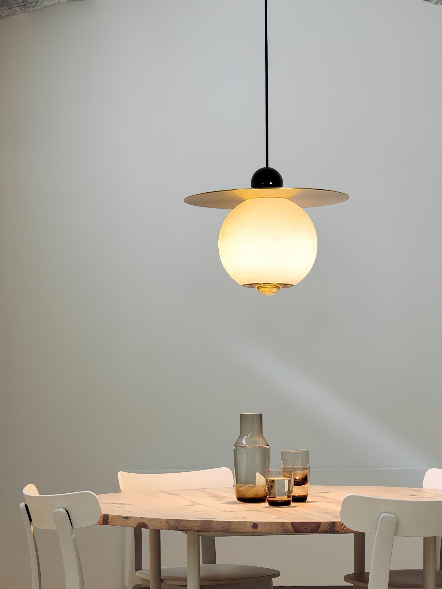 Clérachic Brass and Alabaster Globe Cord Pendant Light above a round pine table with a smoked glass carafe and tumblers.
