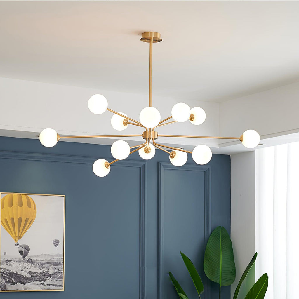 Brass Clérachic chandelier with white globes against a blue panelled wall, with a framed balloon picture and a banana-leaf plant.