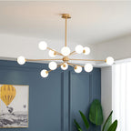 Brass Clérachic chandelier with white globes against a blue panelled wall, with a framed balloon picture and a banana-leaf plant.