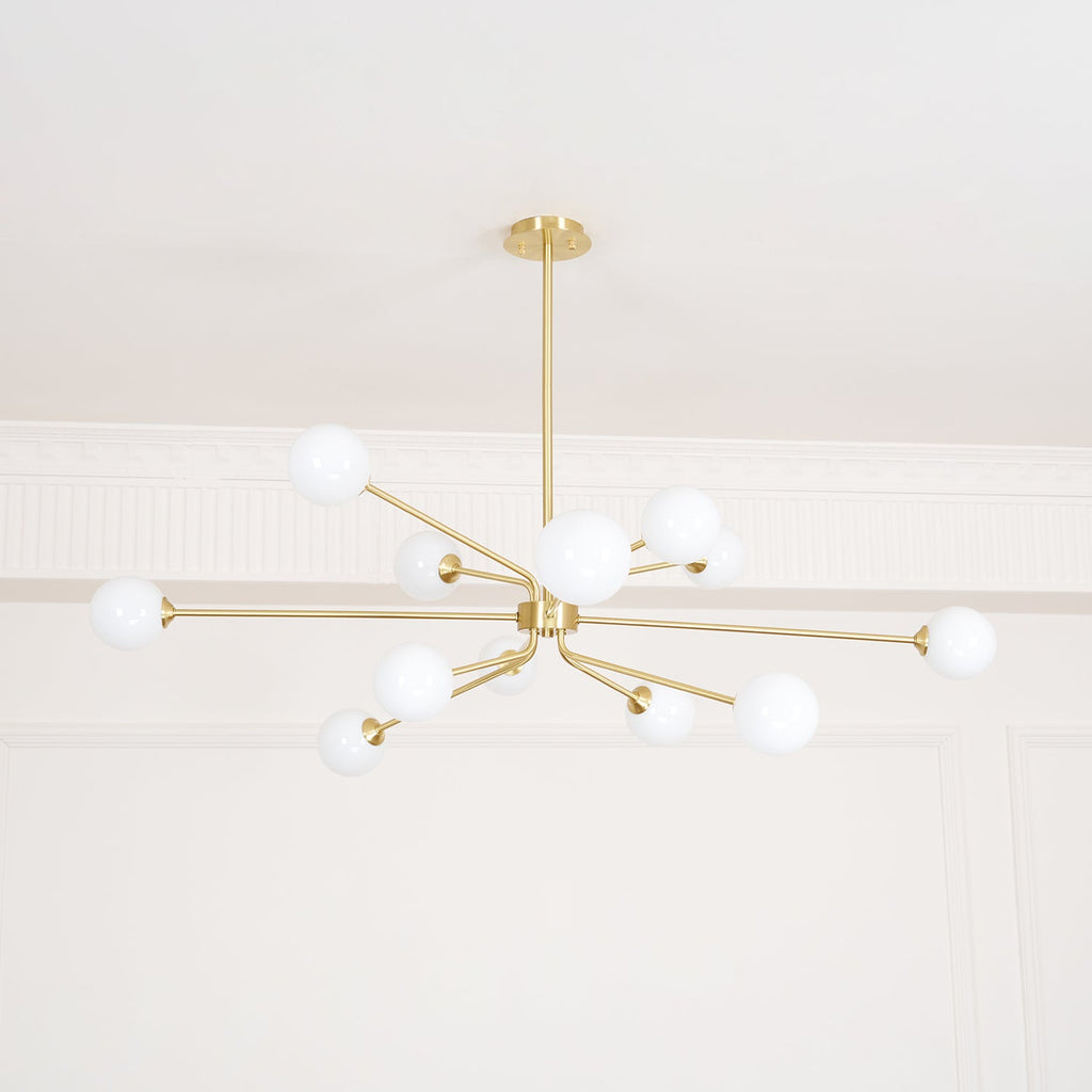 Looking up at a brass Clérachic chandelier with white globes, set against a white ceiling and a moulded cornice.