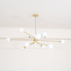 Looking up at a brass Clérachic chandelier with white globes, set against a white ceiling and a moulded cornice.