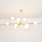 A lit brass Clérachic chandelier with a full spread of white globes, against a pale ceiling and panelled wall.