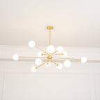 Brass Clérachic chandelier with glowing white globes on long arms, seen below a white ceiling with moulded panels.