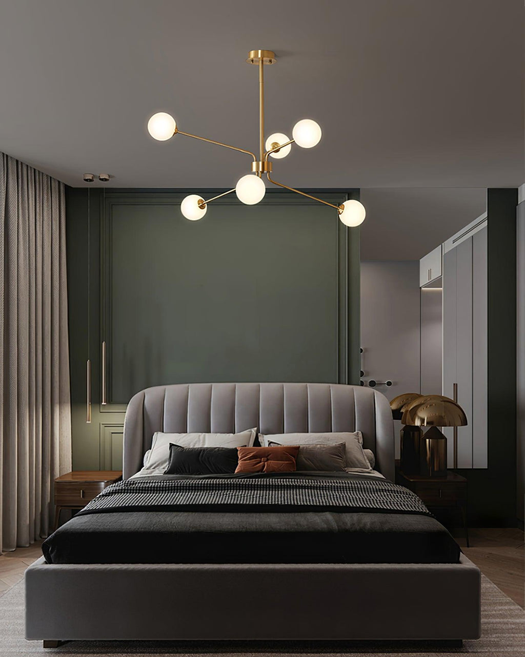Smaller brass Clérachic chandelier with a few white globes hanging above a grey upholstered bed in a green and dark grey bedroom.