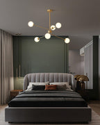 Smaller brass Clérachic chandelier with a few white globes hanging above a grey upholstered bed in a green and dark grey bedroom.