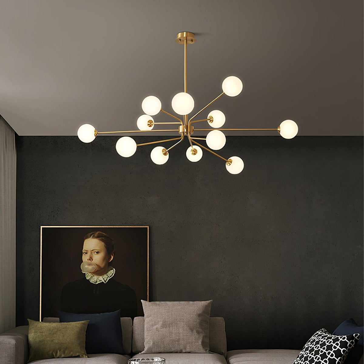 Large brass Clérachic chandelier with white globes above a sofa, with a framed portrait on a dark charcoal wall.