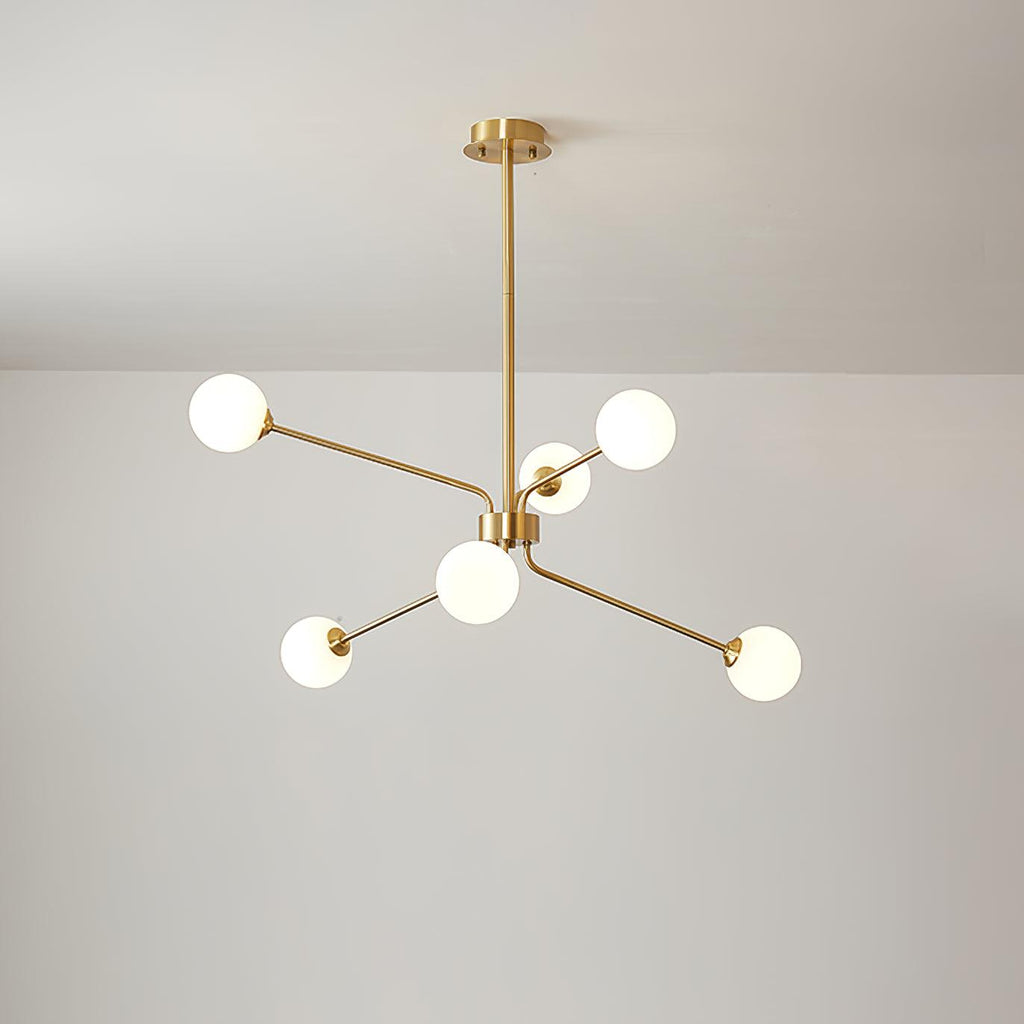 A smaller brass Clérachic chandelier with six white globes on slim arms, hung from a long rod below a pale ceiling.