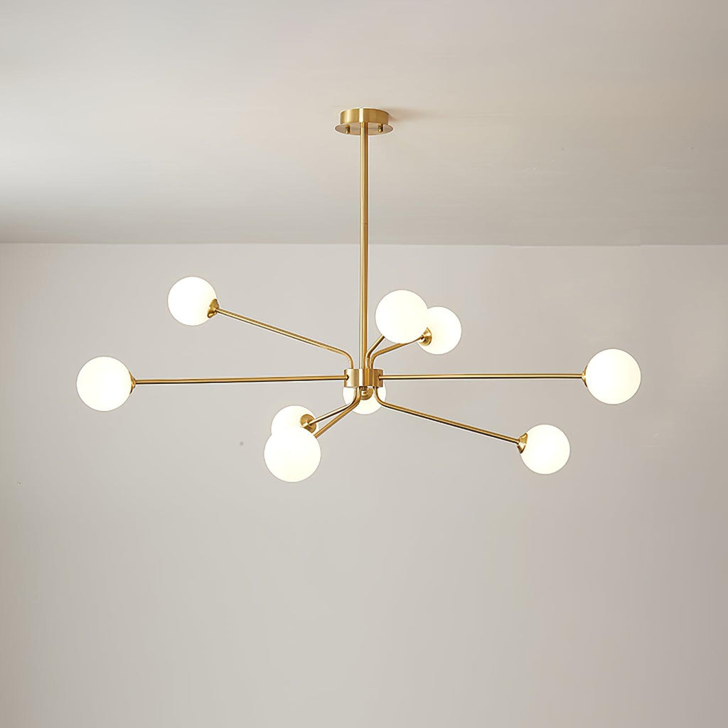 Brass Clérachic chandelier with nine white globes on arms of different lengths, against a plain light wall.