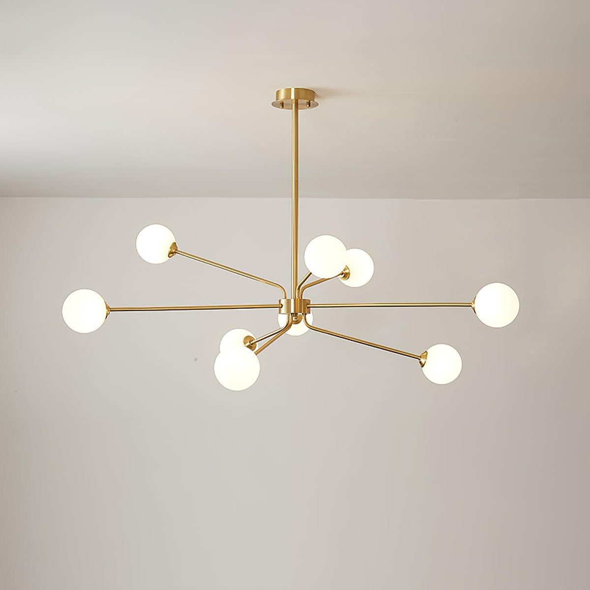 Brass Clérachic chandelier with nine white globes on arms of different lengths, against a plain light wall.