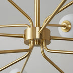 Close view of the brass hub and bent arms of this Clérachic chandelier, with a white globe at the edge of the frame.