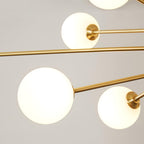 Close view of three frosted white globes and the slim brass arms that hold them on this Clérachic chandelier.