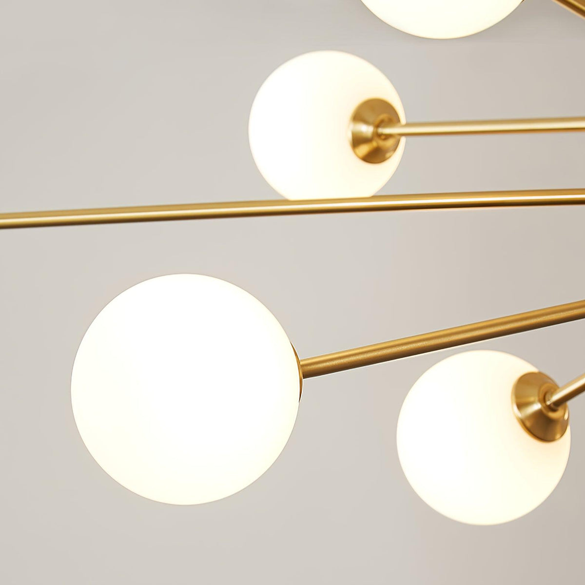 Close view of three frosted white globes and the slim brass arms that hold them on this Clérachic chandelier.