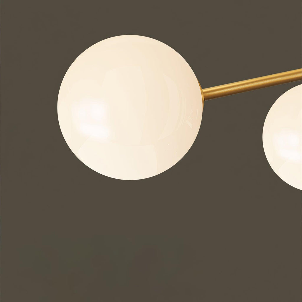 Close view of a single frosted white globe on a brass arm of this Clérachic chandelier, against a dark olive wall.