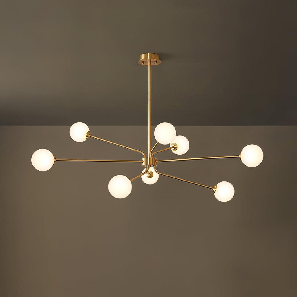 Brass Clérachic chandelier with nine glowing white globes on long arms, in front of a dark olive wall.