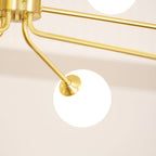 Close view of a brass arm bending down to a white glass globe on this Clérachic chandelier, with a warm glow behind.