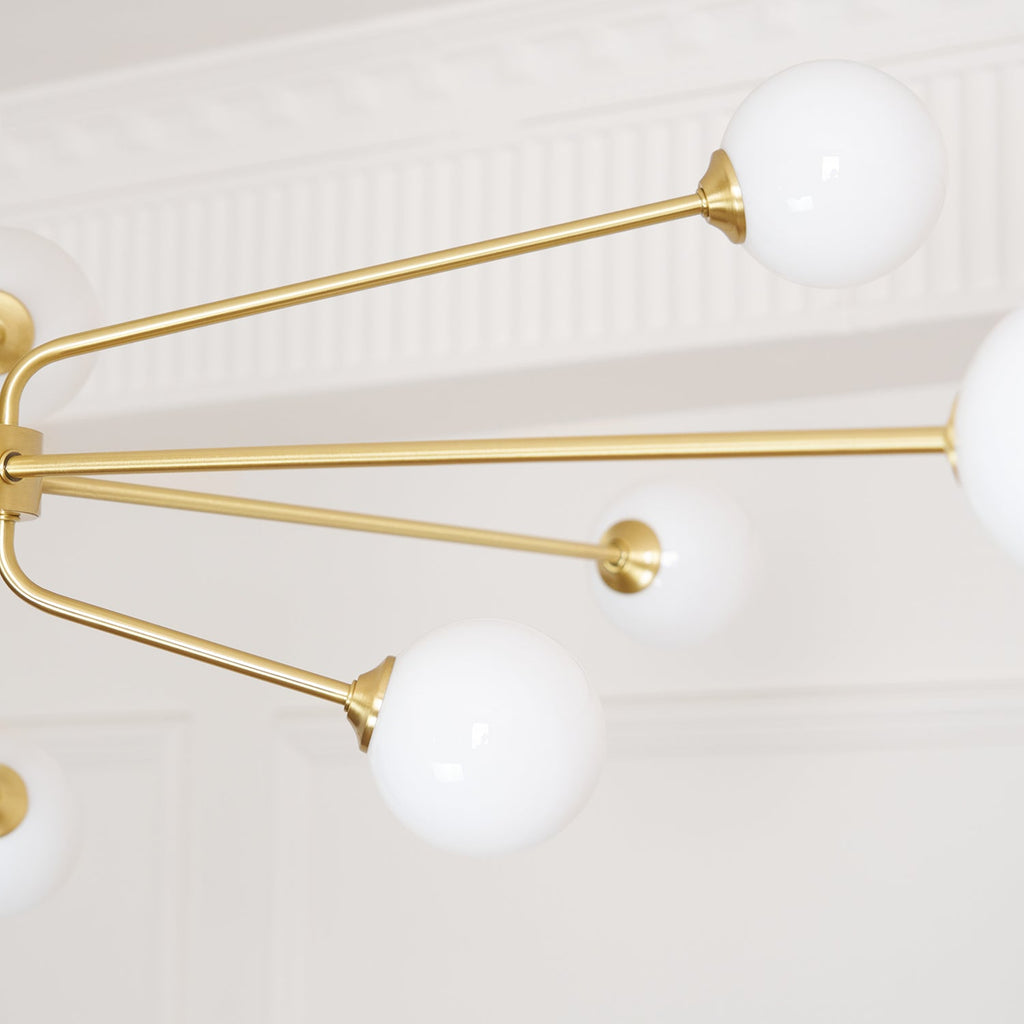 Close view of white glass globes on thin brass arms, with a white moulded cornice behind this Clérachic chandelier.