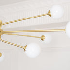 Close view of white glass globes on thin brass arms, with a white moulded cornice behind this Clérachic chandelier.