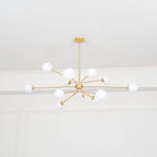 A brass Clérachic chandelier with many arms and white globes hangs below a plain white ceiling, seen from far below.